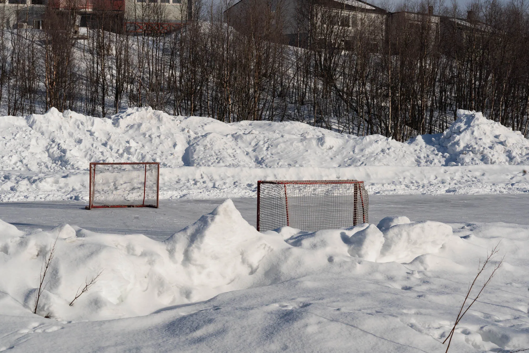 ice field with hockey goals surrounded by big piles of snow