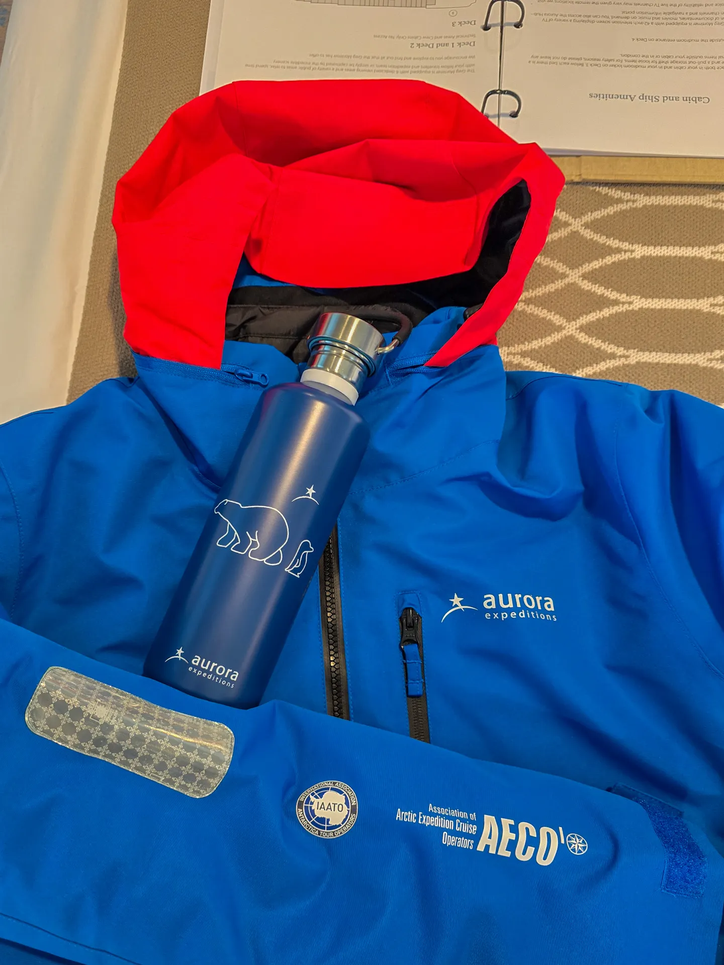 Expedition Jacket, blue with red hood accent, with the Aurora Expeditions and IAATO logos on the sleeve.