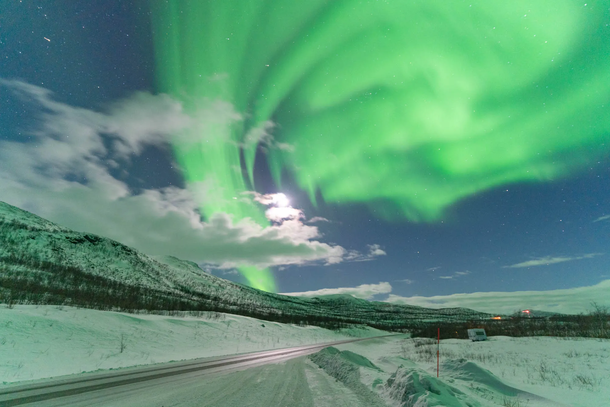 other side of the camera, large aurora coming out behind a street illuminated by moonlight