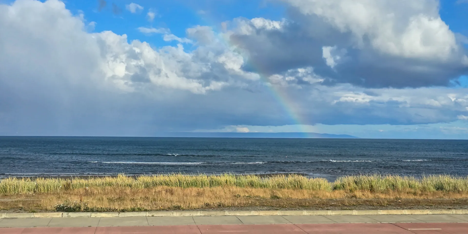 rainbow over the beach at the side of the road