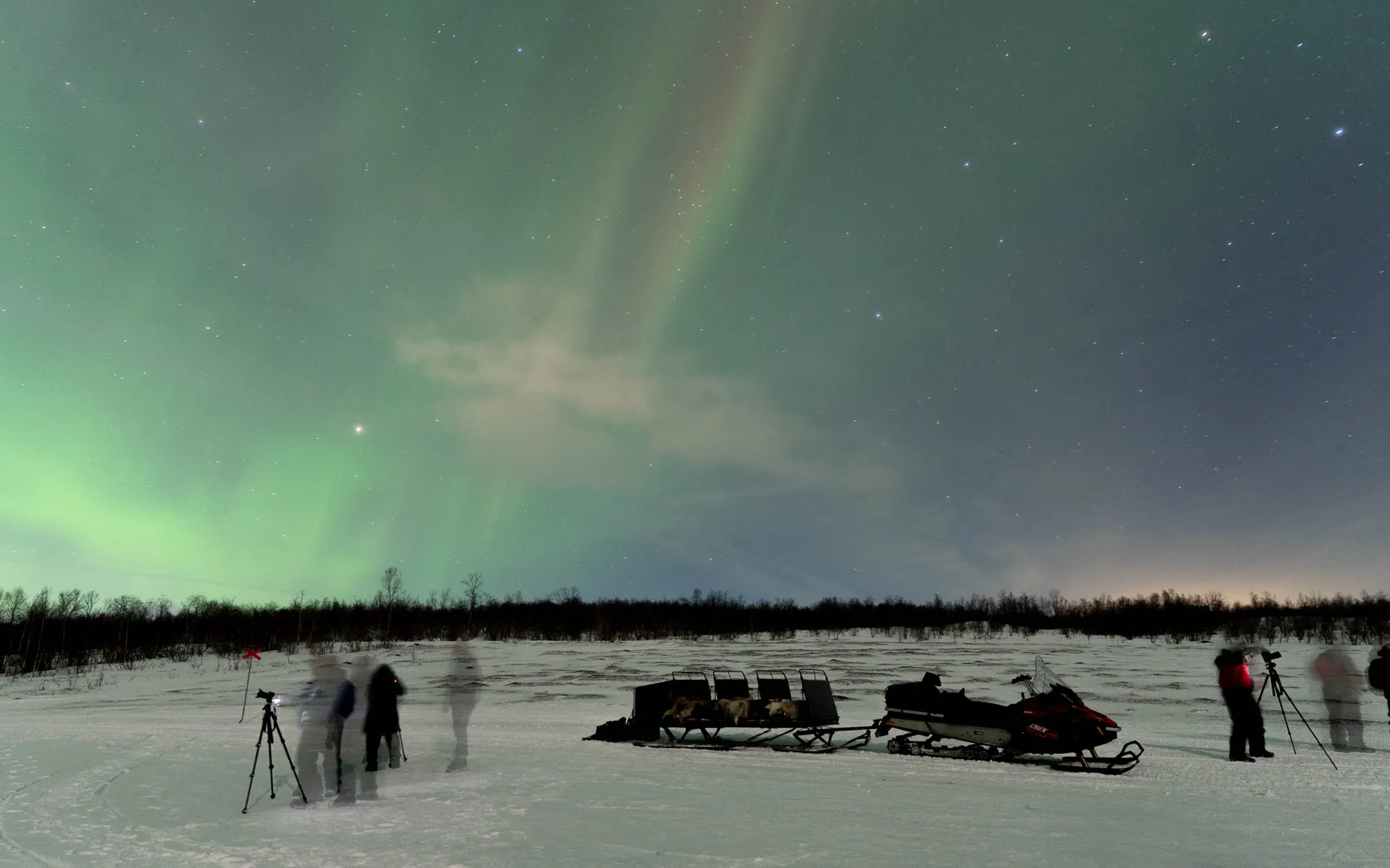 rainbow like faint streak in the sky with snow mobile and moving photographers in the foreground